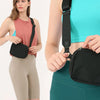 A woman wearing a teal top and green leggings is holding a black cross-body nylon waist bag with a black strap.