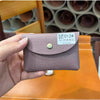A hand holds a mauve leather card holder with a gold stud closure on an orange table.
