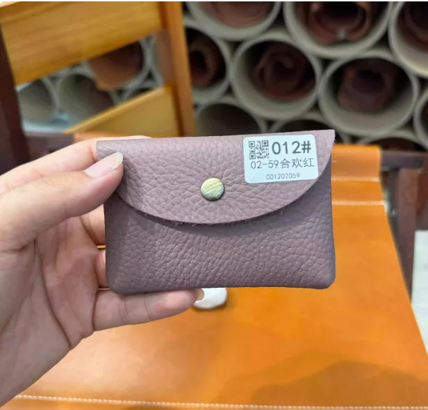 A hand holds a mauve leather card holder with a gold stud closure on an orange table.