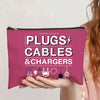 A pink zippered pouch labeled PLUGS CABLES & CHARGERS is held by a person.