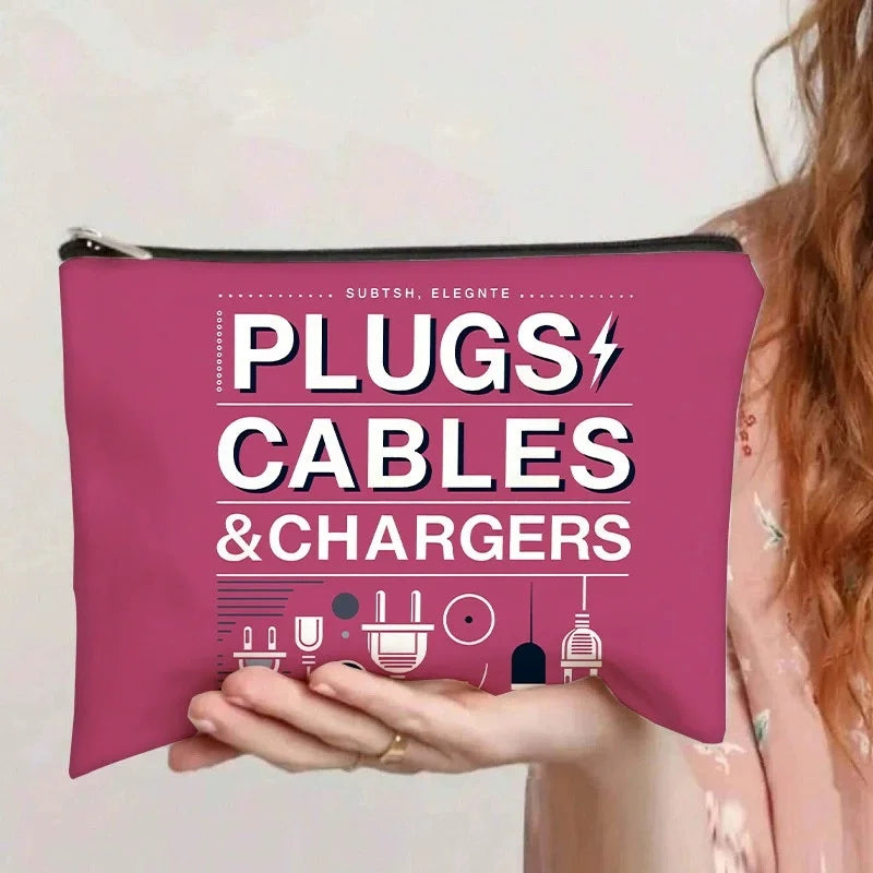 A pink zippered pouch labeled PLUGS CABLES & CHARGERS is held by a person.