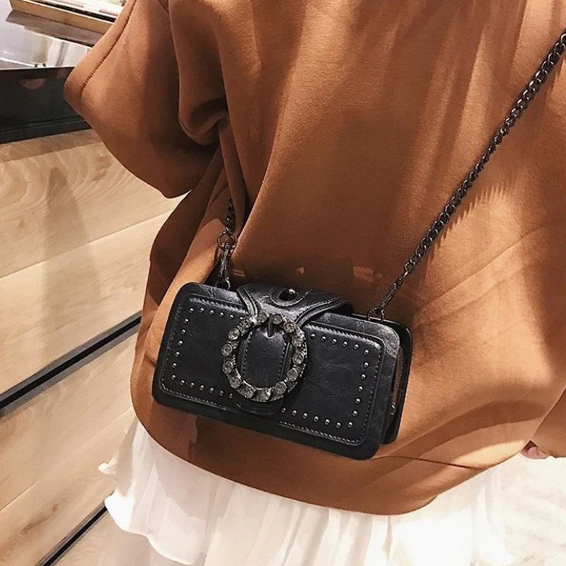 A brown jacket is worn by a person, featuring a black PU leather crossbody bag with a rhinestone buckle.