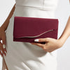 A woman holds a deep burgundy velvet evening clutch against a white dress.