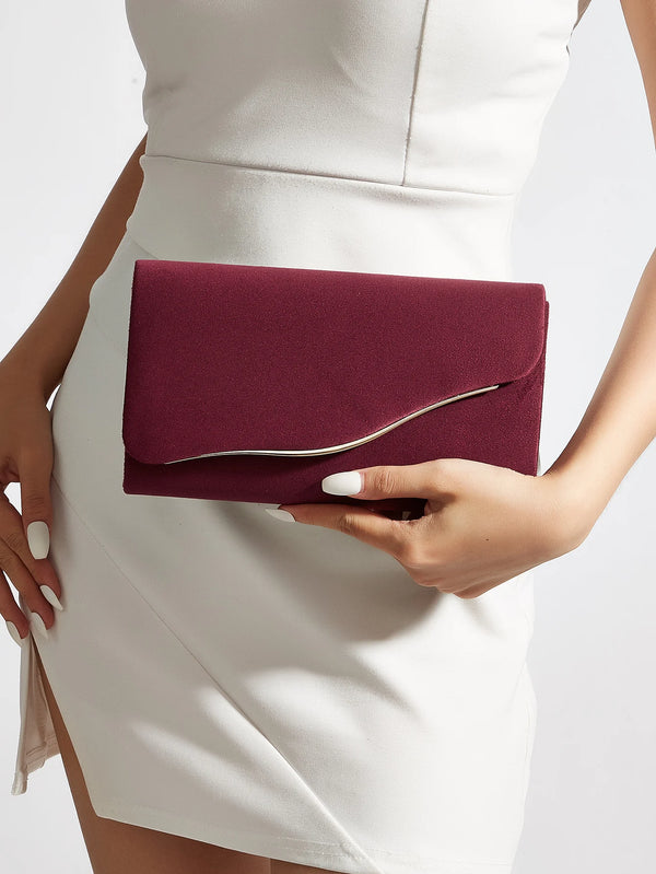 A woman holds a deep burgundy velvet evening clutch against a white dress.