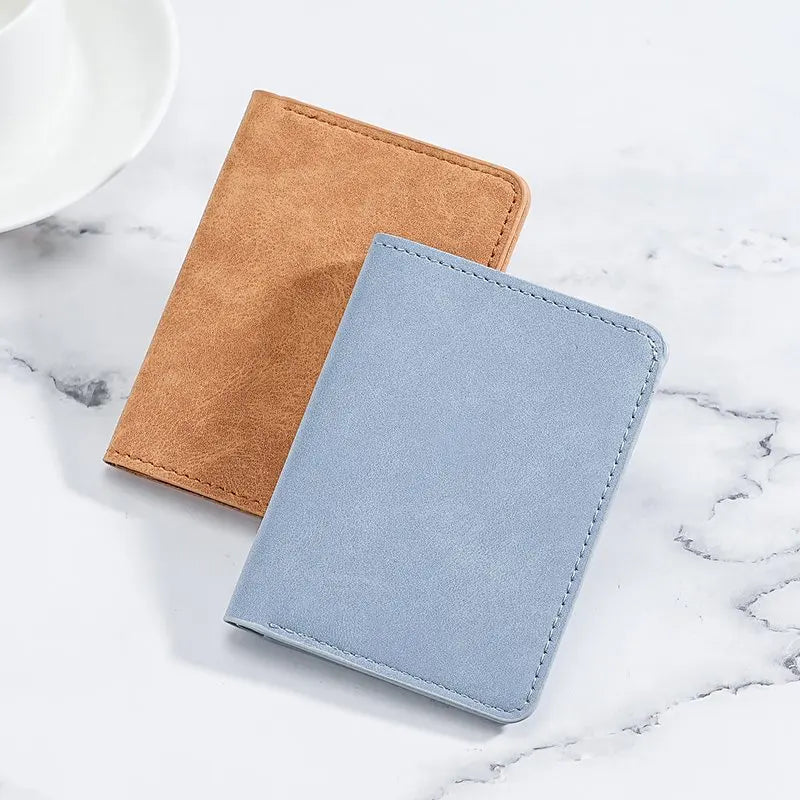 A tan leather card wallet and a light blue leather card wallet resting on a white marble surface.
