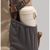 A white insulated water bottle is visible inside a gray fabric pouch attached to a tan backpack strap.