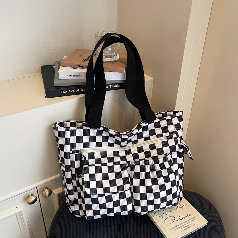 A black and white checkered corduroy tote bag resting on a light-colored shelf.