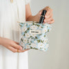 A hand holds a floral canvas makeup bag with the text DIDF BAG and a black eyeliner pencil.
