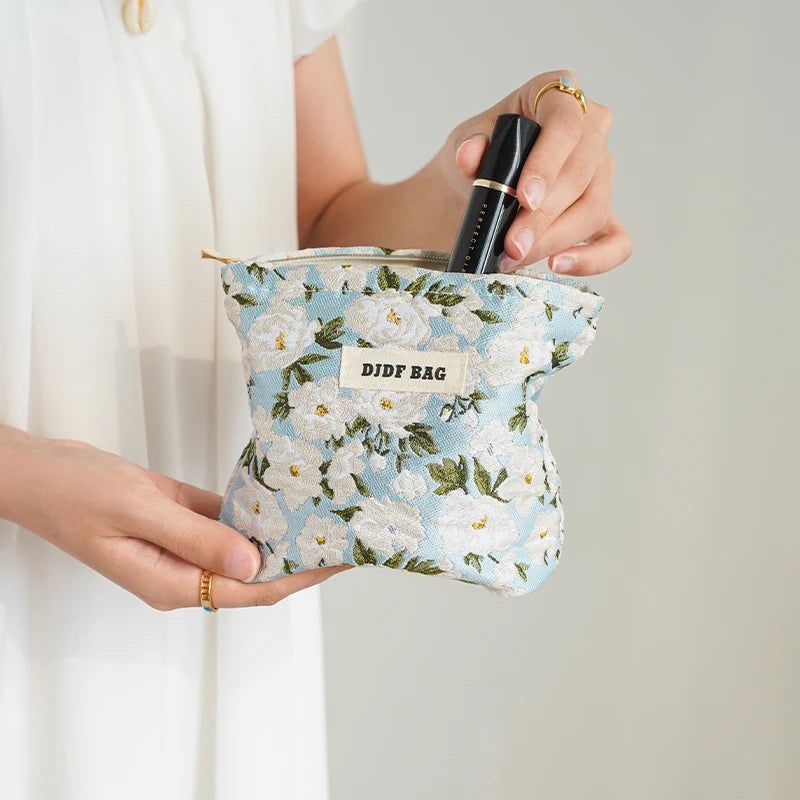 A hand holds a floral canvas makeup bag with the text DIDF BAG and a black eyeliner pencil.