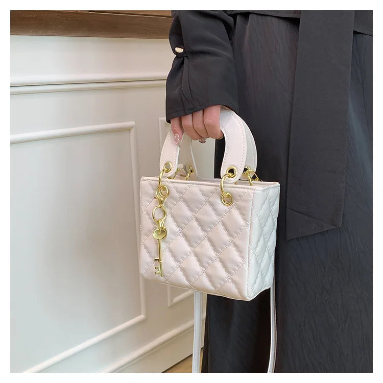 A woman holds a light pink quilted diamond grid crossbody bag with gold hardware against a white background.