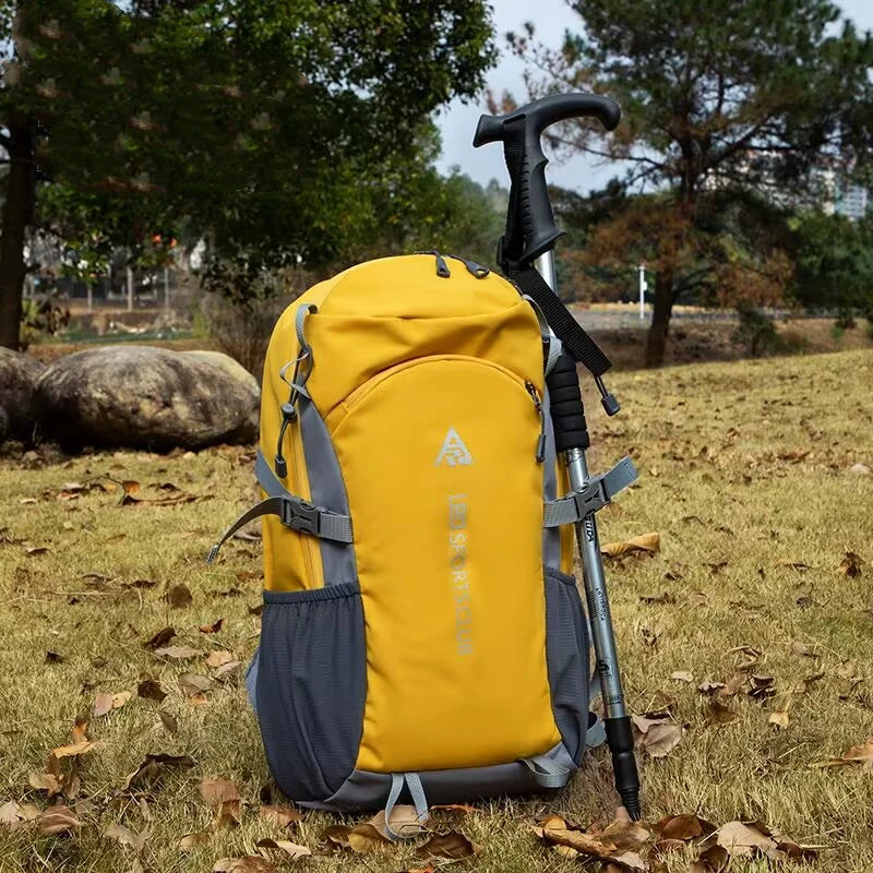 A yellow and gray durable 80L waterproof hiking backpack resting on dry grass.