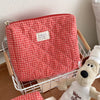 A red and white plaid cosmetic storage bag is shown inside a white wire basket.