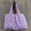 A purple reusable shopping bag featuring a pattern of small black cats on a light background.