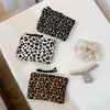 A collection of leopard print cosmetic bags and a silver makeup brush displayed on a white surface.