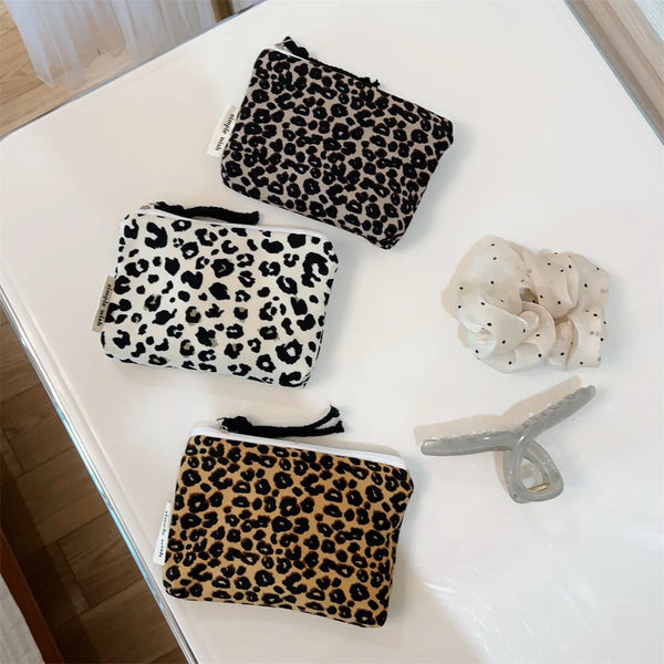 A collection of leopard print cosmetic bags and a silver makeup brush displayed on a white surface.
