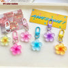 A collection of 12 colorful resin flower keychains in various shades of pink, purple, blue, and yellow displayed on a white t