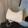 A light beige leather shoulder bag with a gold zipper and strap is held by a person against a blurred background.