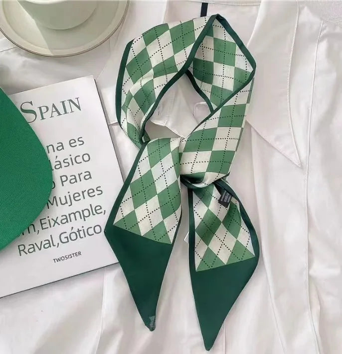 Écharpe de soie à carreaux vert foncé et blanc nouée, présentée sur un t-shirt blanc avec un livre.