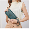 A woman holds a dark teal RFID anti-theft multi-card wallet with a leather wrist strap against a cream top and beige skirt.