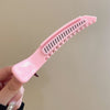 Une main tient une pince à cheveux rose professionnelle antidérapante avec de fines dents pour le coiffage.