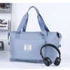 A light blue expandable travel organizer bag with shoulder straps next to a pair of black headphones.