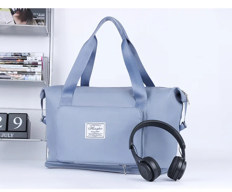 A light blue expandable travel organizer bag with shoulder straps next to a pair of black headphones.