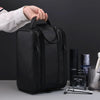 A black PU leather travel toiletry bag with organizer pockets is being held by a hand on a gray surface.