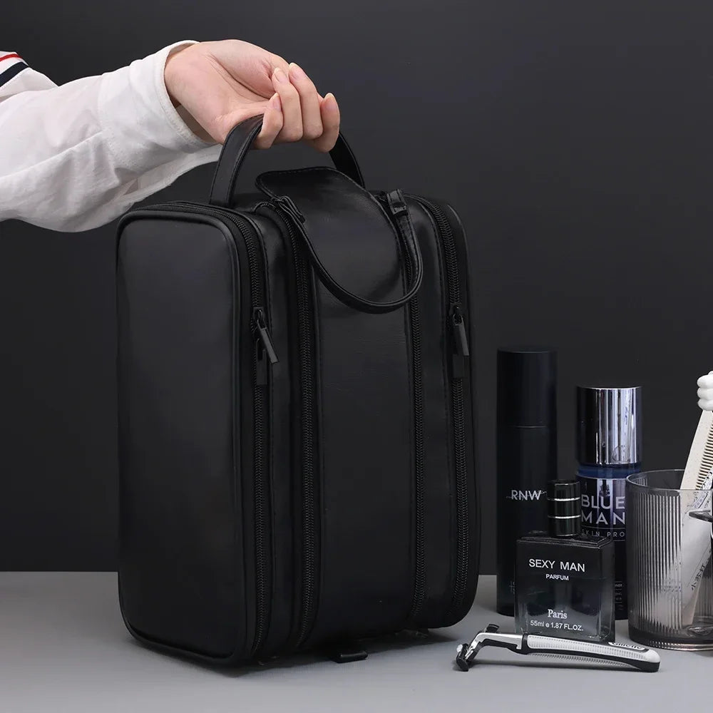 A black PU leather travel toiletry bag with organizer pockets is being held by a hand on a gray surface.