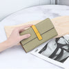 A beige genuine cow leather bifold wallet with a yellow accent is shown resting on a light wooden board next to a magazine.
