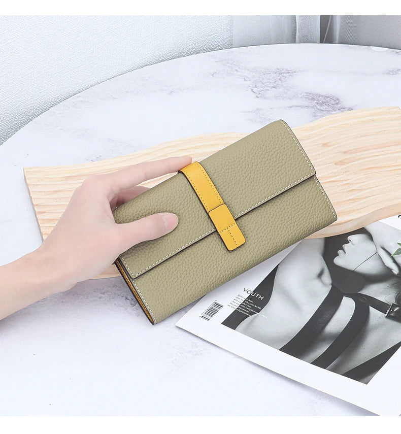 A beige genuine cow leather bifold wallet with a yellow accent is shown resting on a light wooden board next to a magazine.