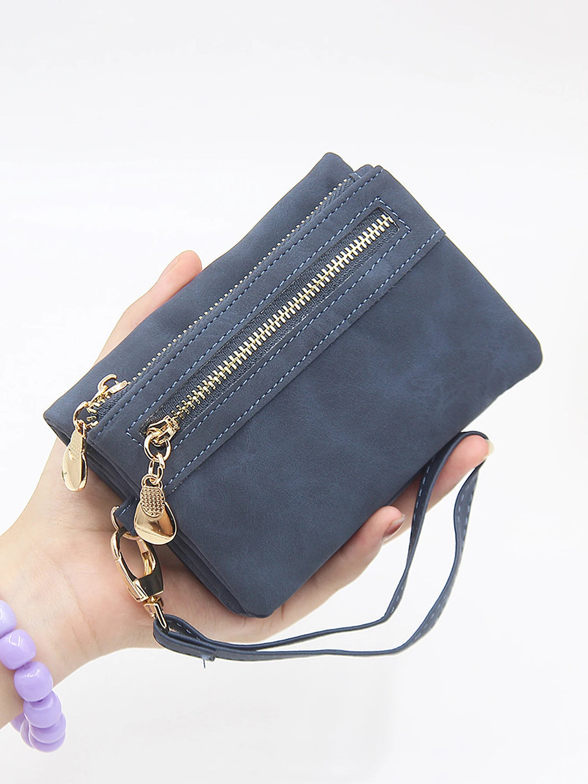 A hand holds a dark blue retro PU leather double fold wallet with a gold zipper and leather strap.