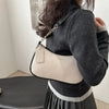 A close-up shot of a beige crescent crossbody bag with a gold chain strap worn by a person.