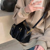 A person holds a black vintage PU leather shoulder bag with gold hardware against a light brown hoodie.
