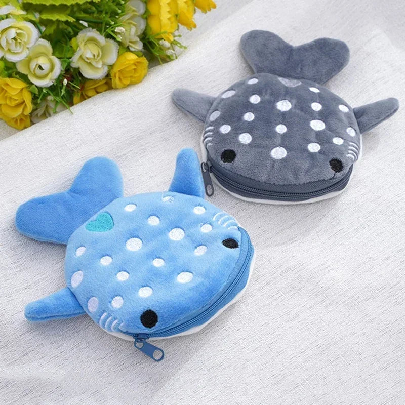 A cute blue shark mini plush coin purse wallet resting on a white fabric with yellow flowers.