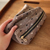 Une main tient une pochette de rangement cosmétique en tissu brun à pois blancs et une fermeture éclair noire sur une surface