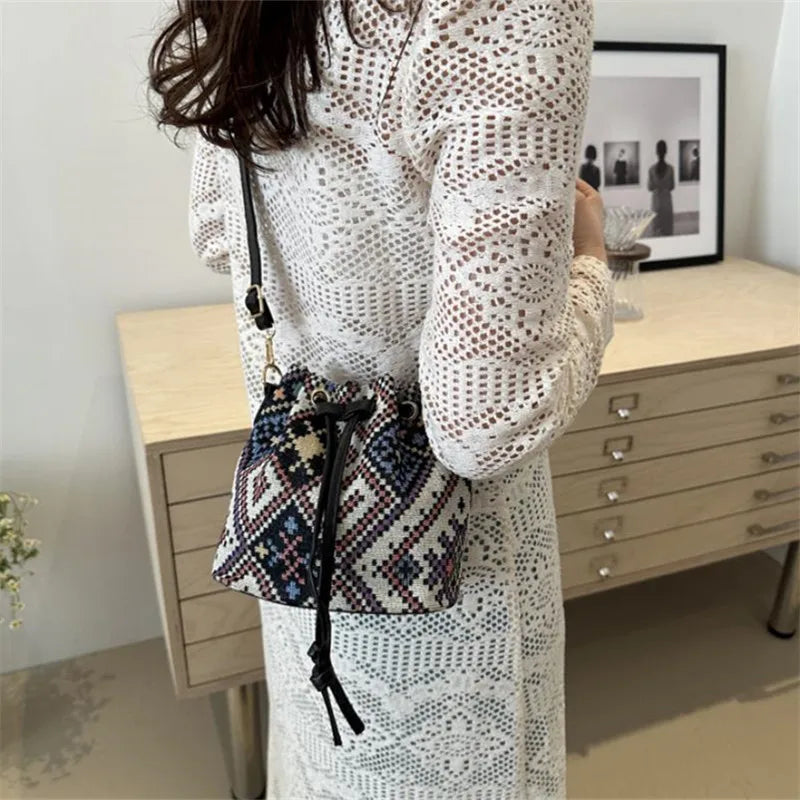 A woman holds a floral patterned drawstring bucket bag in black and white on her arm.