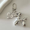 Silver balloon dog keychain charm with a heart tag and jump ring on a white surface