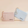 A light pink wallet and a light blue wallet are displayed next to each other on a beige surface.