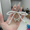 A hand holds a silver Y2K bowknot pearl keychain with white pearls on a string.