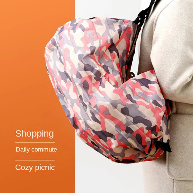 A camouflage patterned foldable nylon storage bag with a black strap is shown being carried by a person.