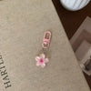 A pink resin flower keychain with a silver ring attached, resting on a beige surface.