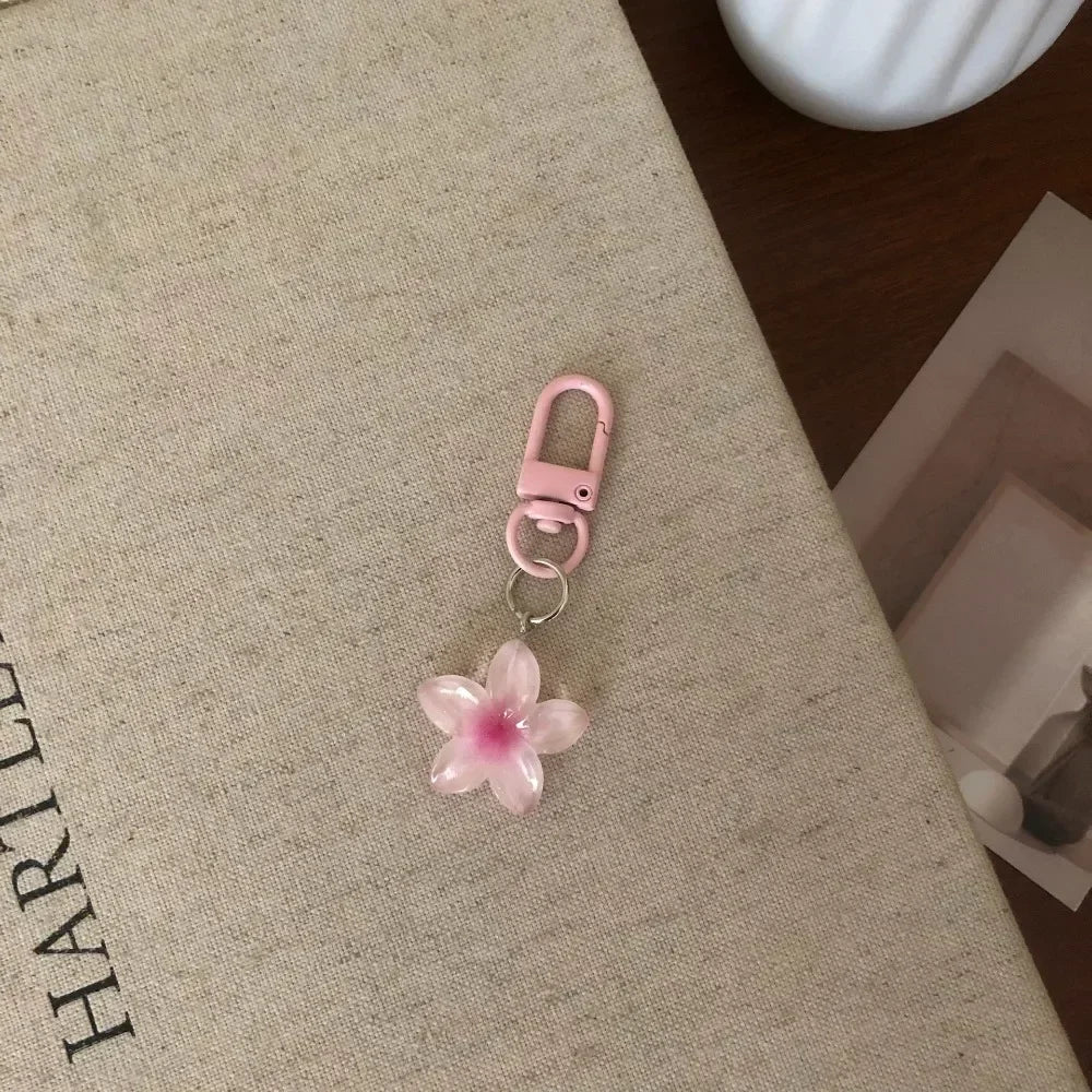 A pink resin flower keychain with a silver ring attached, resting on a beige surface.