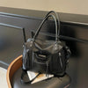 Bolso cruz de cuero suave negro de lujo con herrajes plateados sobre una superficie oscura.