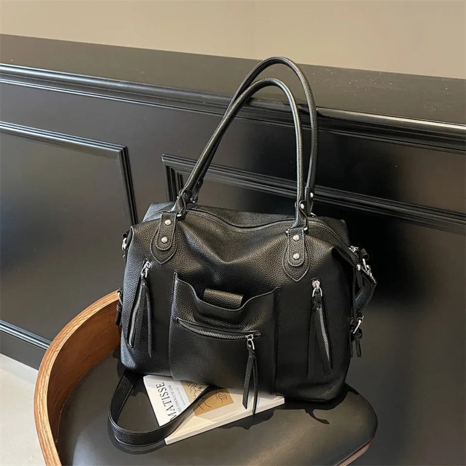 Bolso cruz de cuero suave negro de lujo con herrajes plateados sobre una superficie oscura.