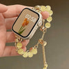 Eine Hand hält ein verstellbares Metallarmband mit blassgelben Kristallperlen und ein Smartphone.