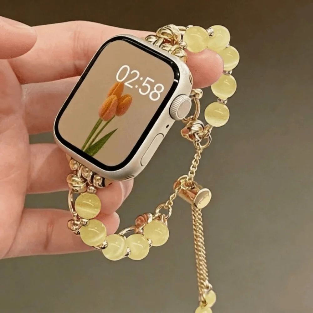 Eine Hand hält ein verstellbares Metallarmband mit blassgelben Kristallperlen und ein Smartphone.