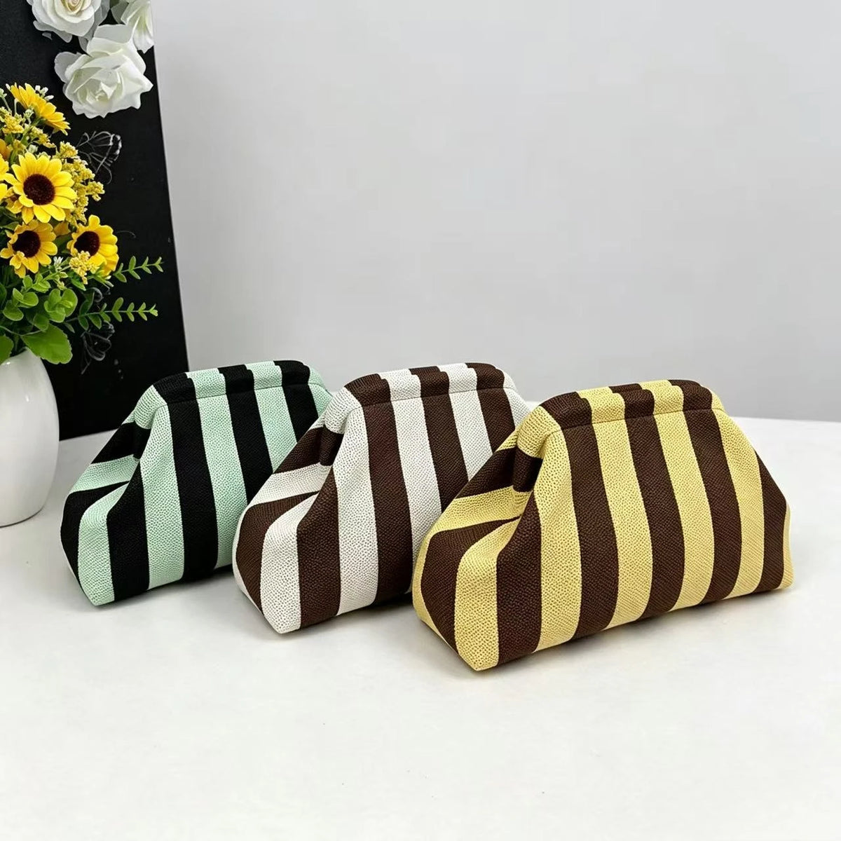 Three striped knit cloud makeup bags in black, green, and gold colors displayed on a white surface.