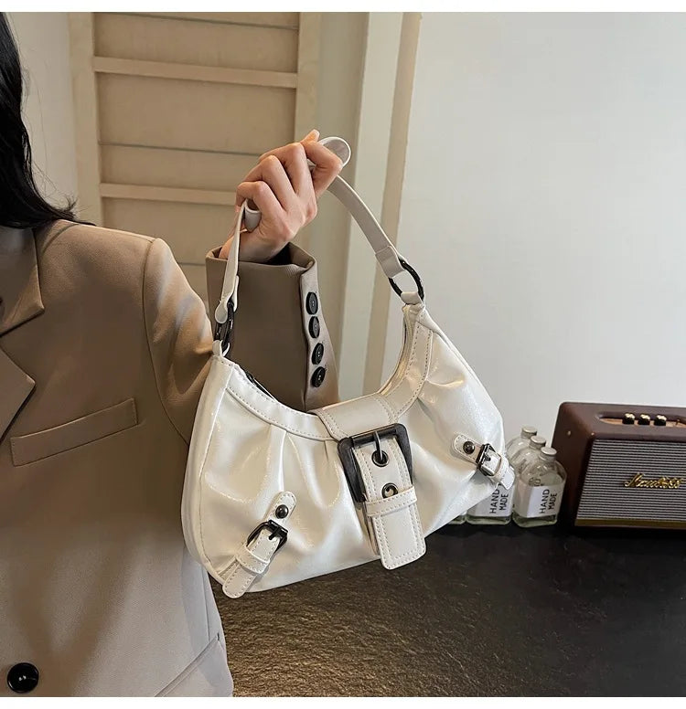 Nahaufnahme einer weißen plissierten Schultertasche mit schwarzem Hardware, die von einer Person gehalten wird.