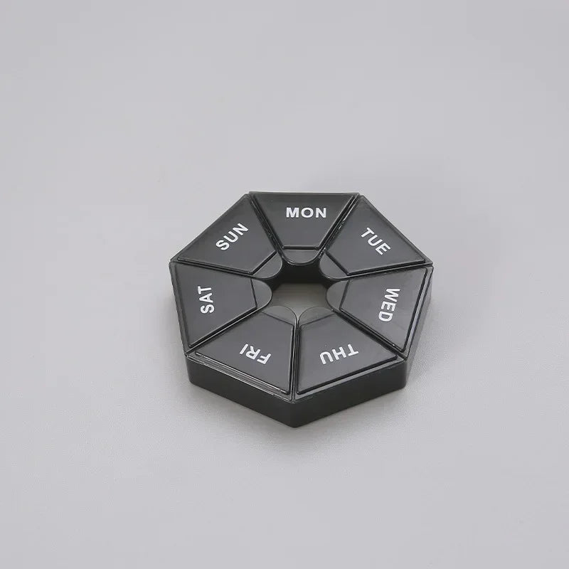 A black, hexagonal weekly pill organizer divided into seven sections labeled with the days of the week.