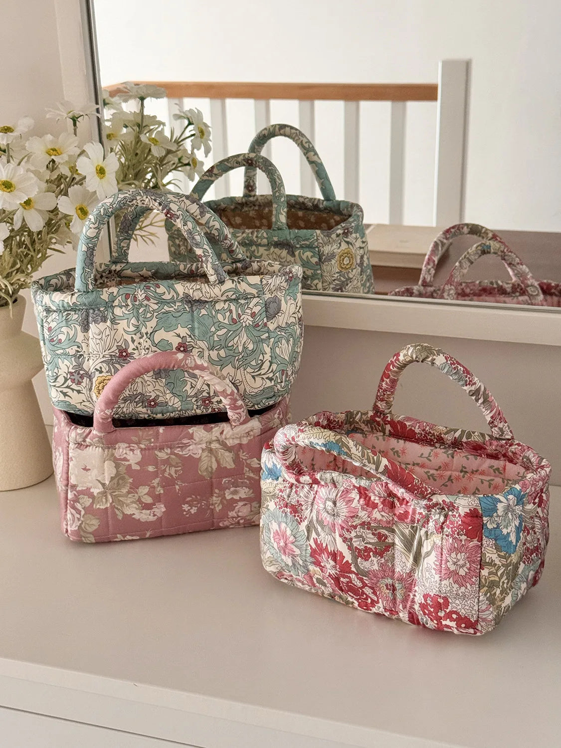 A collection of quilted fabric storage baskets in various floral patterns and pink tones displayed on a white shelf.